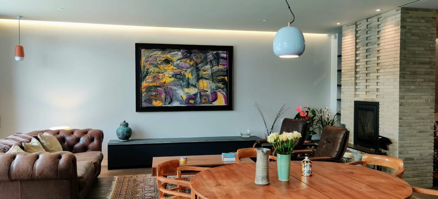 A framed abstract in yellow, violet and black above a long low sideboard in a client's open-plan living and dining room